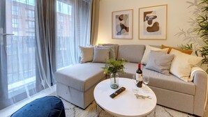 Un saló modern amb un sofà, una taula de centre rodona, un ram de flors, una ampolla de vi i un comandament a distància.