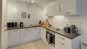 Una cuina moderna amb armaris blancs, forn integrat, un rentaplat i una encimera plena d'aparells.