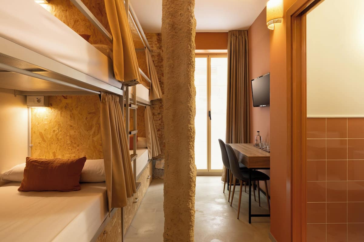 Una habitación de hotel compacta con literas, una zona de comedor y un televisor.