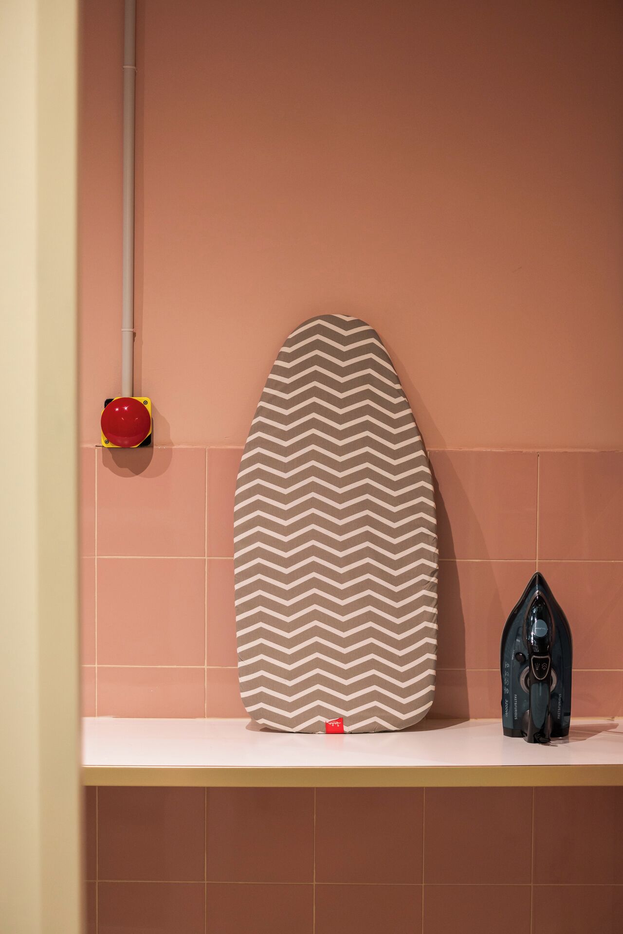 A bathroom with a white countertop, a patterned towel, a red and yellow cleaning tool, and a black hairdryer.