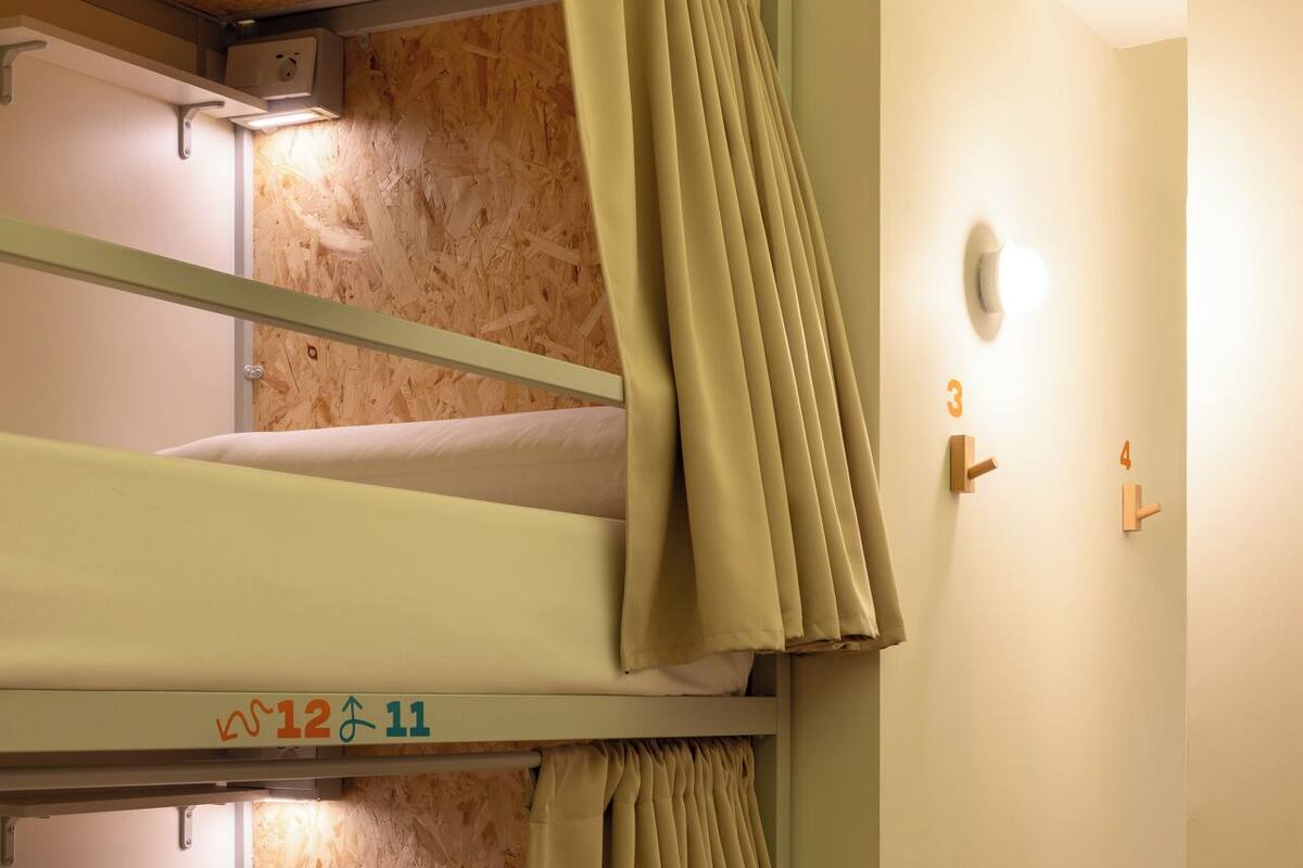 Habitación con literas, pared de madera, un interruptor de luz y una puerta con números.