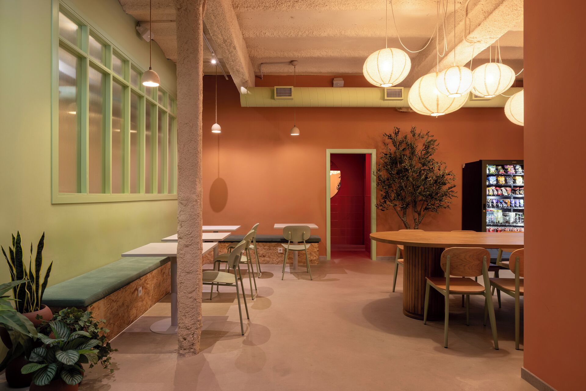 Un café acogedor con una mesa y sillas de madera, una zona de estar con un banco y una máquina expendedora.