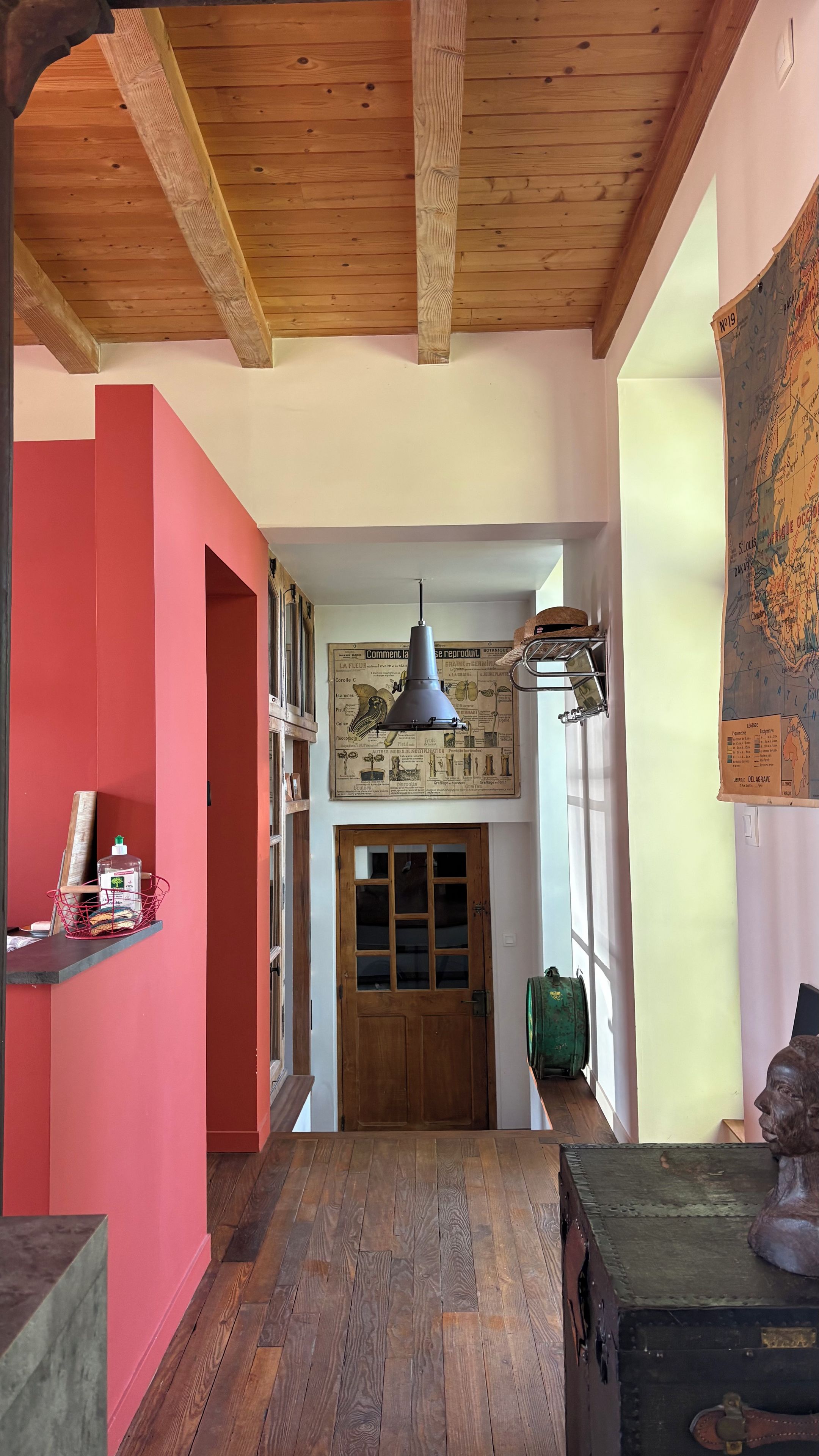A hallway with a wooden ceiling, a red wall, a wooden door, and a map on the wall.