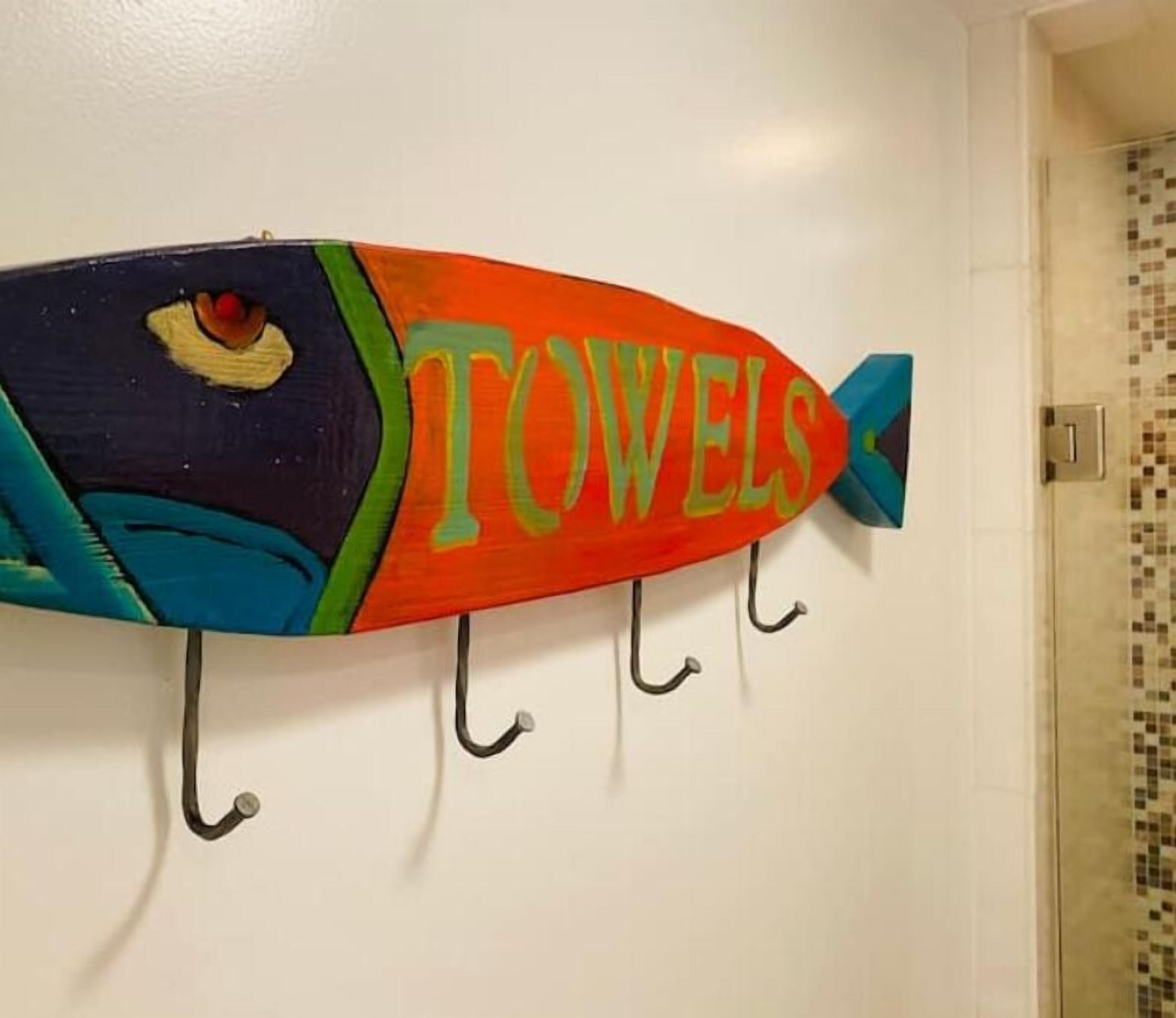 A colorful fish-shaped towel rack with the word "TOWELS" on it, mounted on a wall.