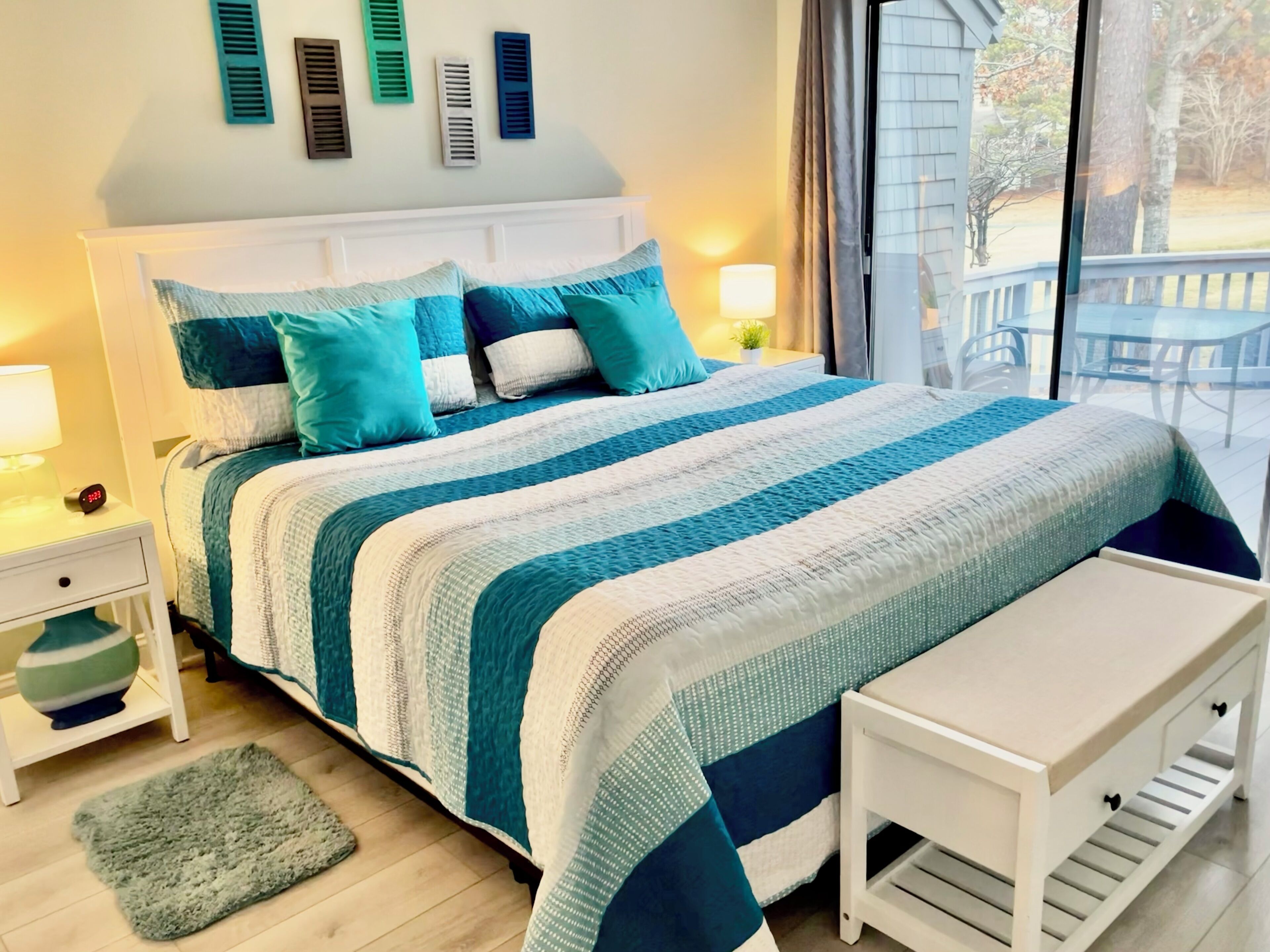 A neatly made bed with a striped blanket, a bedside table with a lamp, a small rug, and a bench.