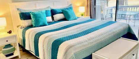 A neatly made bed with a striped blanket, a bedside table with a lamp, a small rug, and a bench.