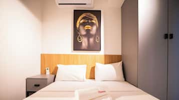 Ein Hotelzimmer mit einem Bett, einem Nachttisch, einer Wand-Klimaanlage und einem gerahmten Kunstwerk über dem Bett.