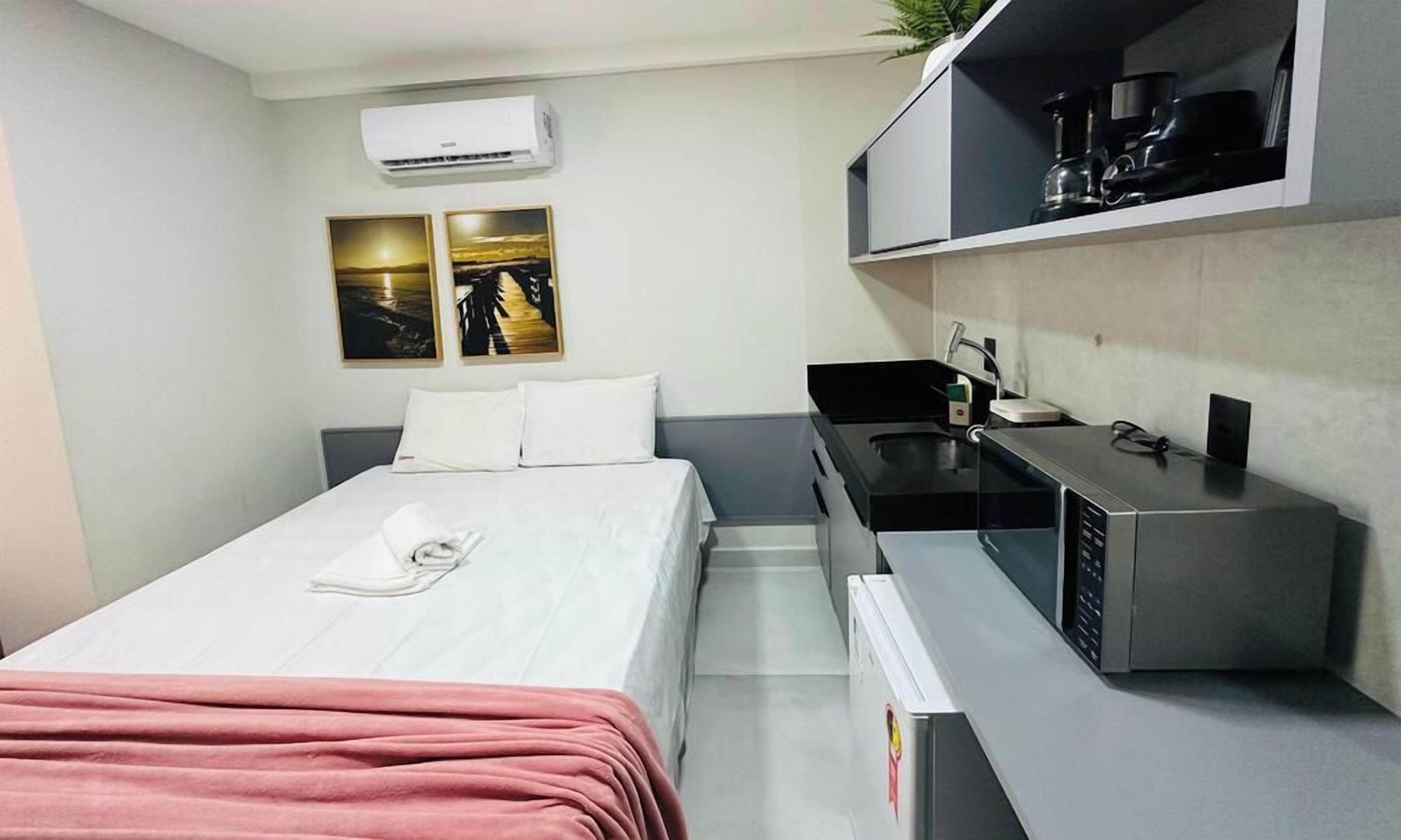 A hotel room with a bed, a small kitchenette, and a wall-mounted air conditioner.
