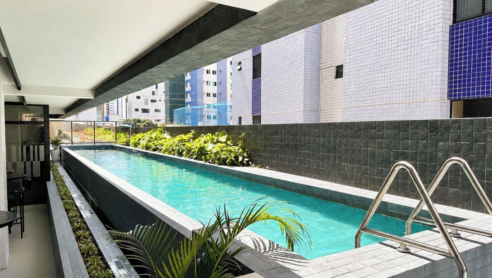 A swimming pool with a metal ladder, surrounded by a tiled wall and plants.