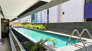 Piscina con una escalera metálica, rodeada de un muro de azulejos y plantas.