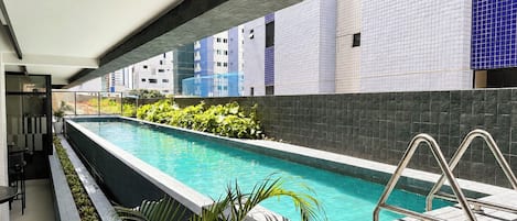 A swimming pool with a metal ladder, surrounded by a tiled wall and plants.