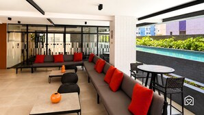 A modern lounge area with a sofa, tables, and a view of a swimming pool. - Co-House (João Pessoa)