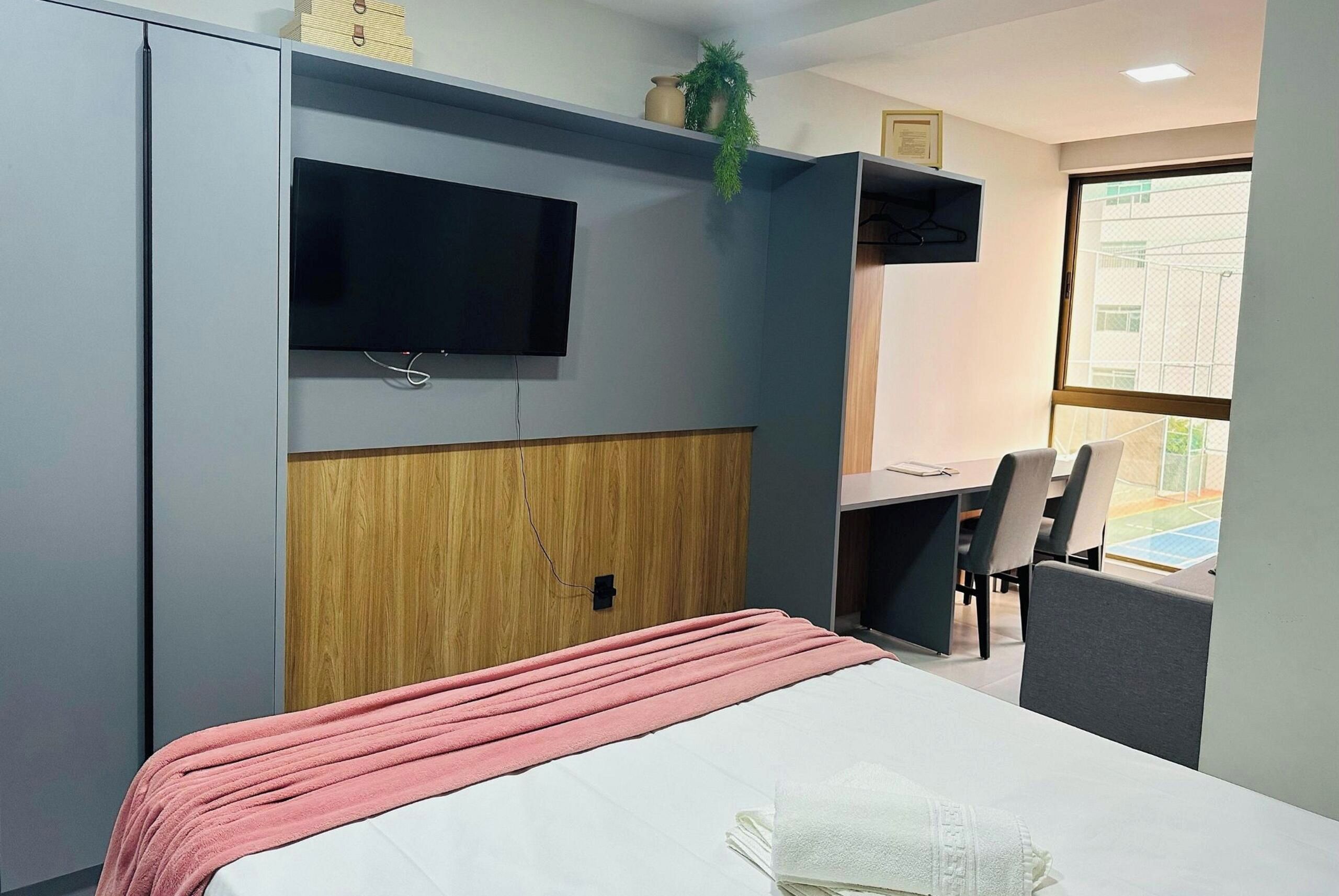 A hotel room with a bed, a desk, a chair, a television, and a window.