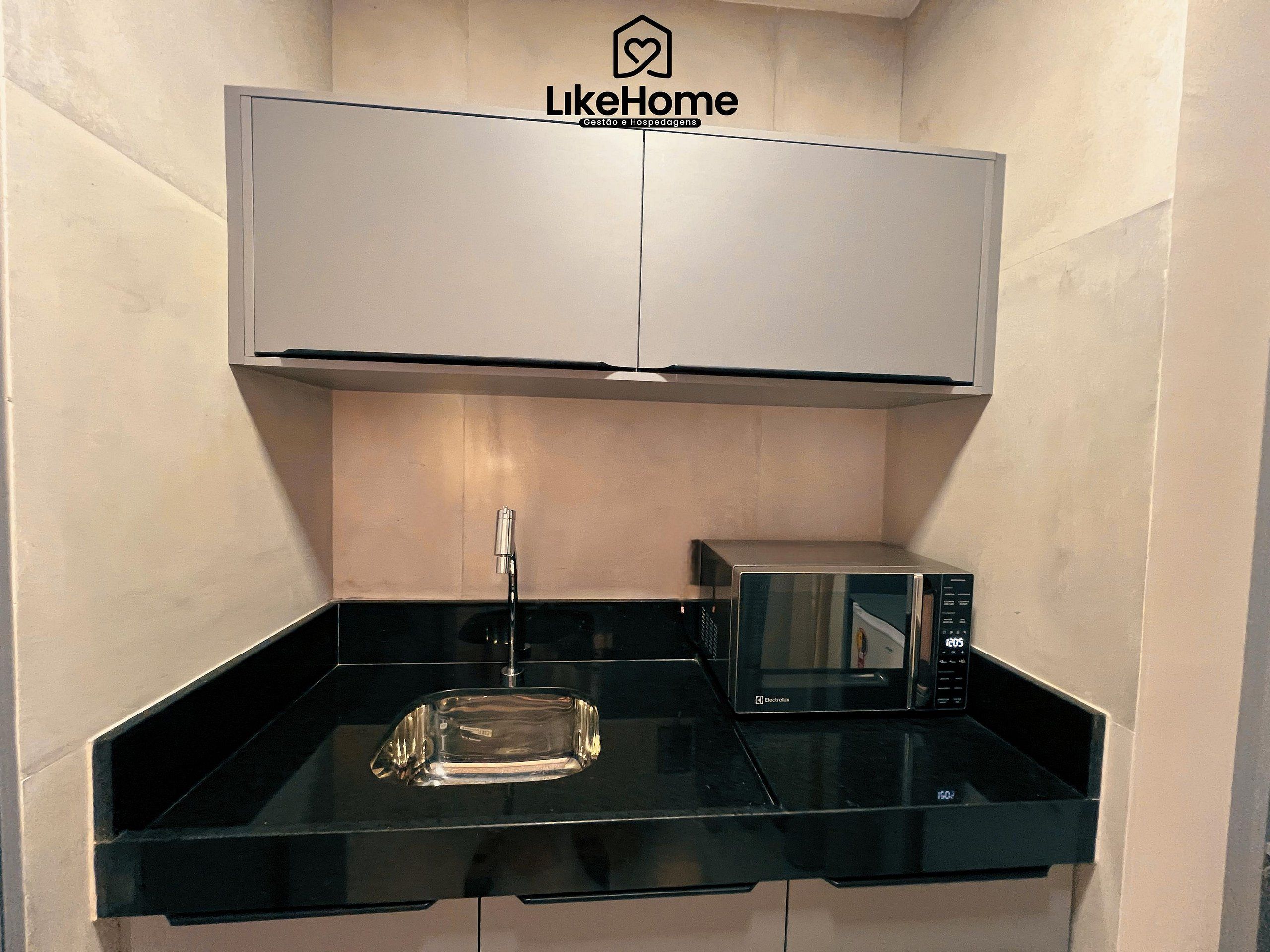 A compact kitchen with a microwave, a sink, and a glass container on the countertop.
