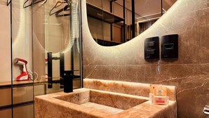 Un baño con lavamanos de mármol, ducha de mano e iluminación integrada en el espejo.