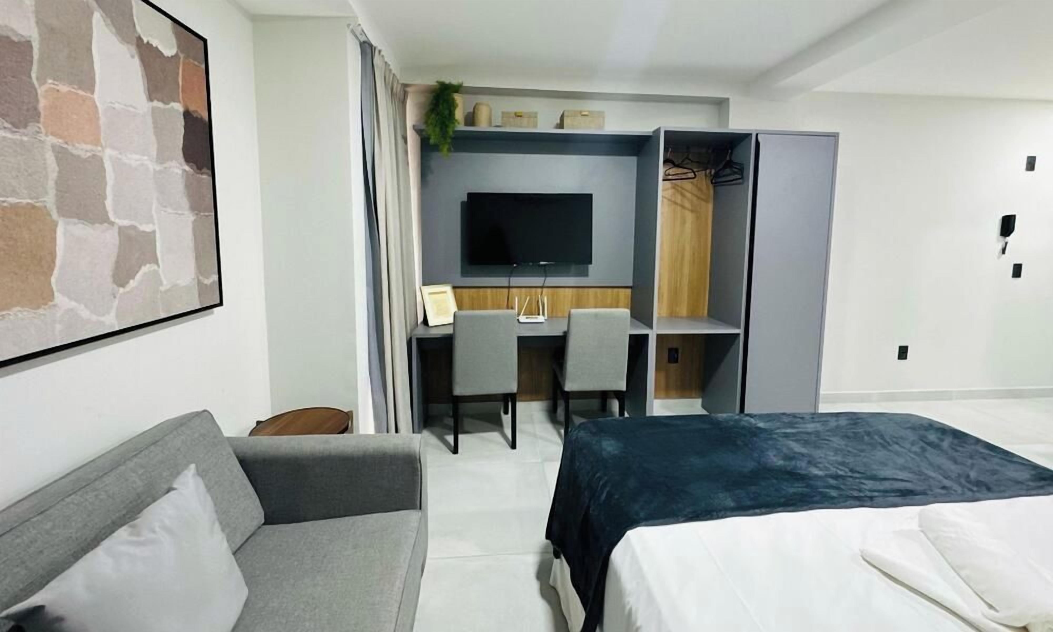 Une chambre d’hôtel moderne équipée d’un lit, d’un canapé, d’un bureau avec une chaise, d’une télévision et d’une armoire.