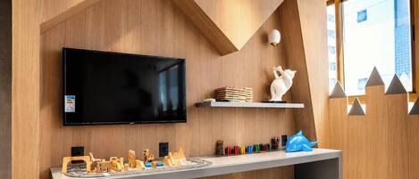 A modern living room with a flat-screen TV, wooden toys, and a white cat statue.