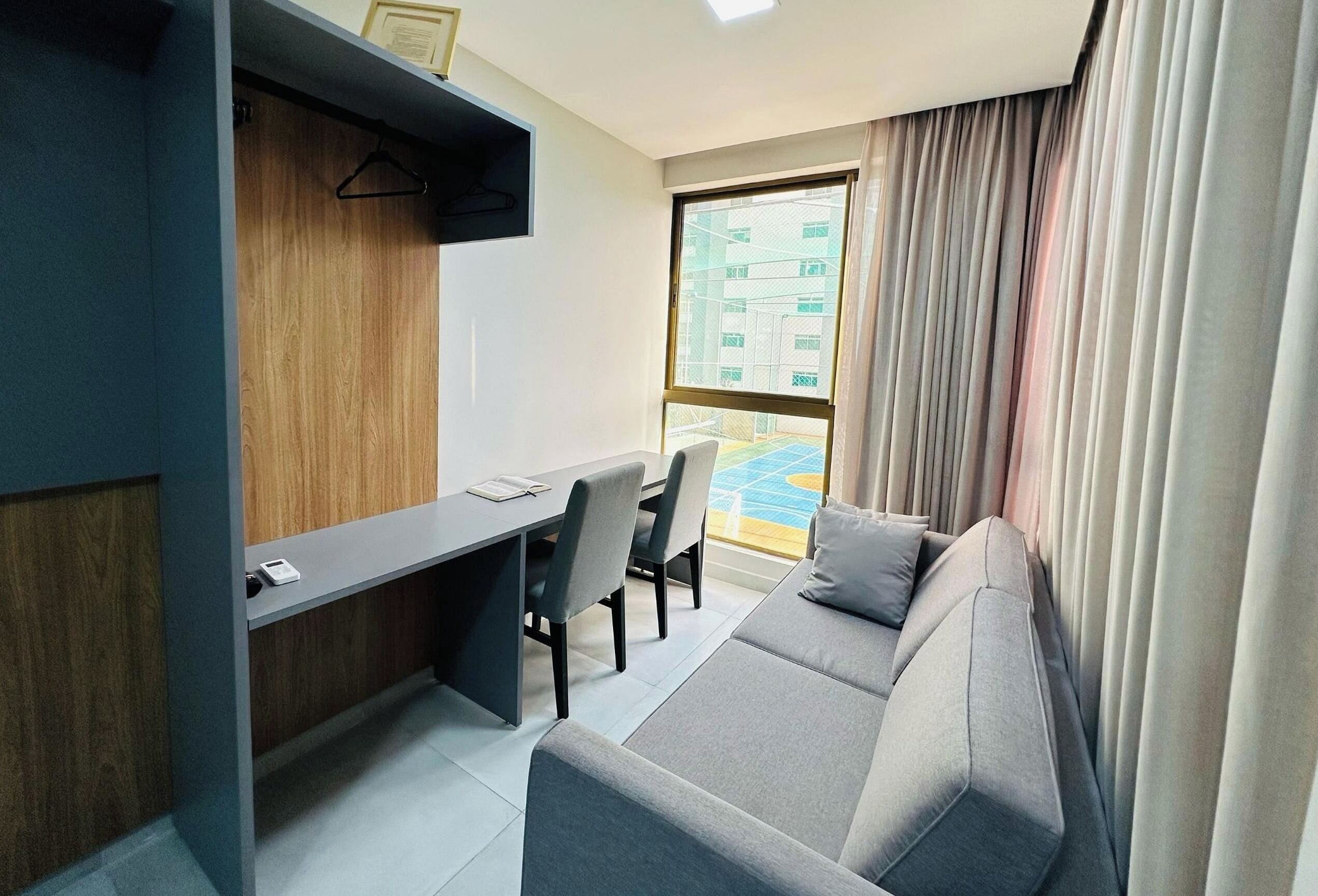 A modern room with a grey sofa, a small desk, and a window with curtains.