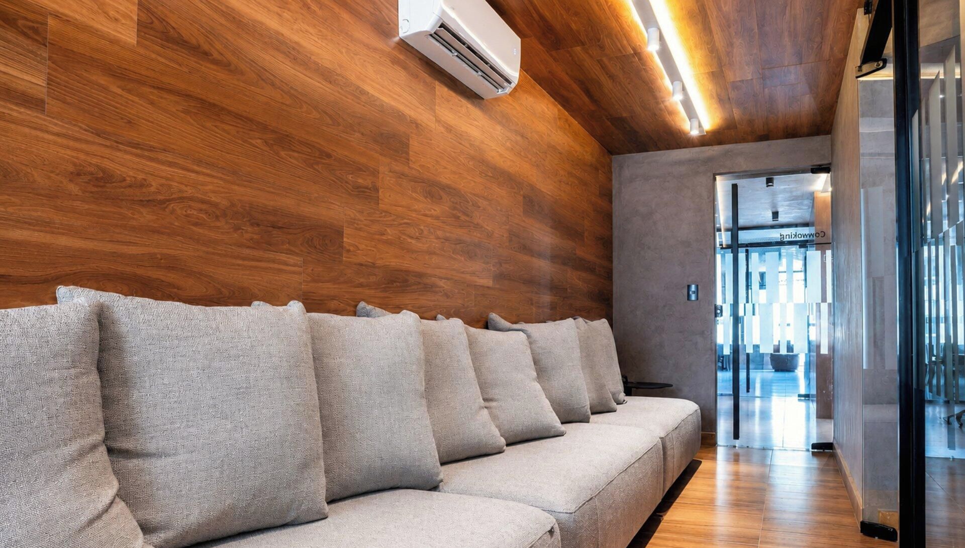Un área de espera moderna con un muro de madera, un sofá con cojines y un equipo de aire acondicionado.