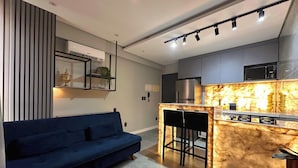A modern kitchen with a marble countertop, a built-in microwave, and a stainless steel refrigerator. - Co-House (João Pessoa)