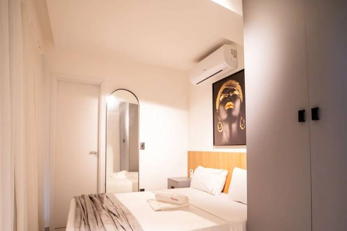 Una habitación de hotel con una cama, una mesita de noche, un espejo y un equipo de aire acondicionado.