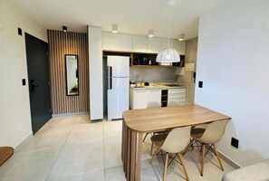 A modern kitchen with a dining area, featuring a wooden table and chairs, a refrigerator, and a hanging light fixture. - Co-House (João Pessoa)