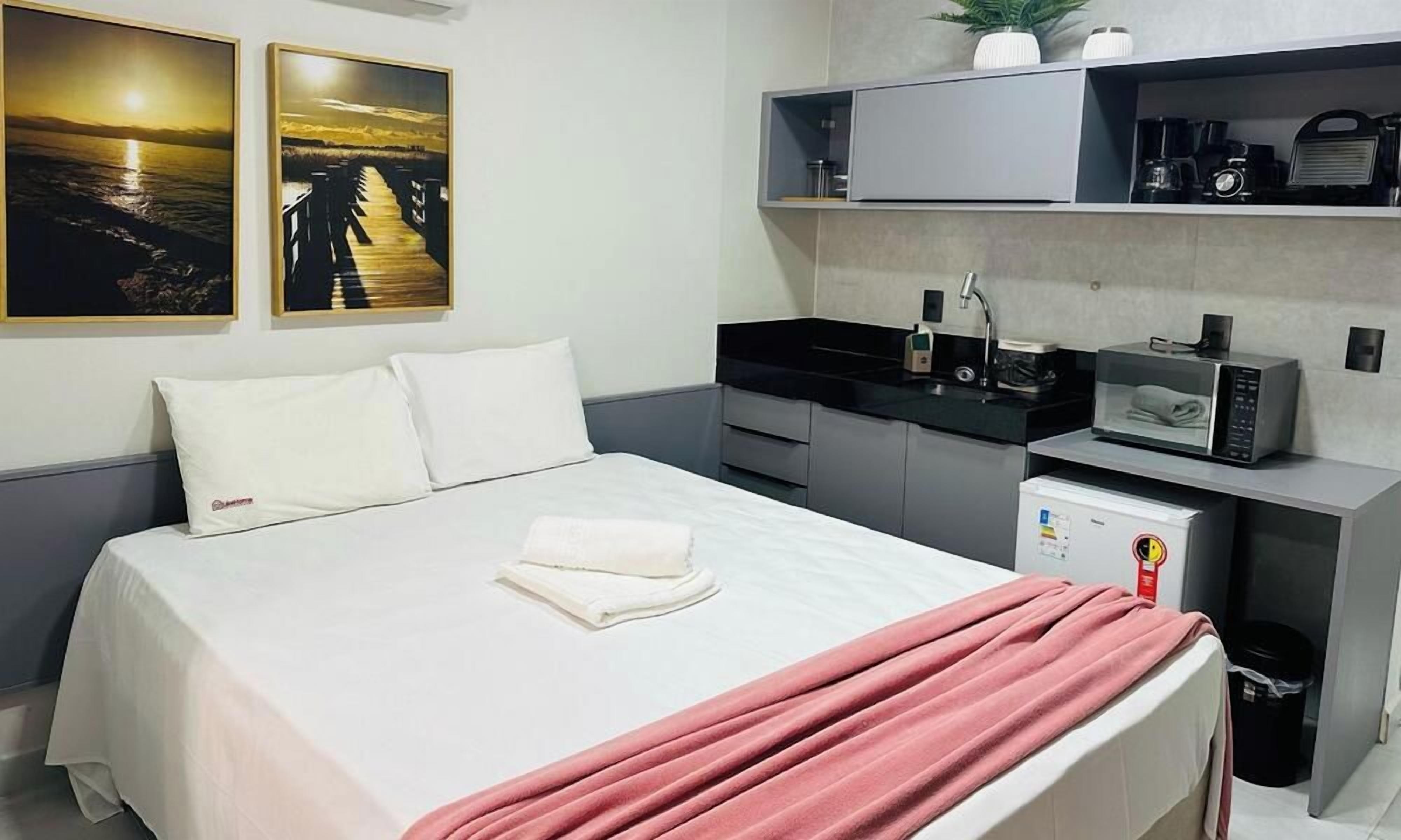 A hotel room with a bed, a microwave, a small kitchen area, and a shelf with a plant.