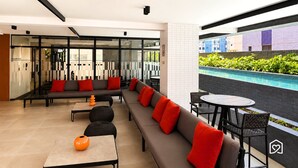 Un área lounge moderna con sofá, mesas y vista a una piscina.