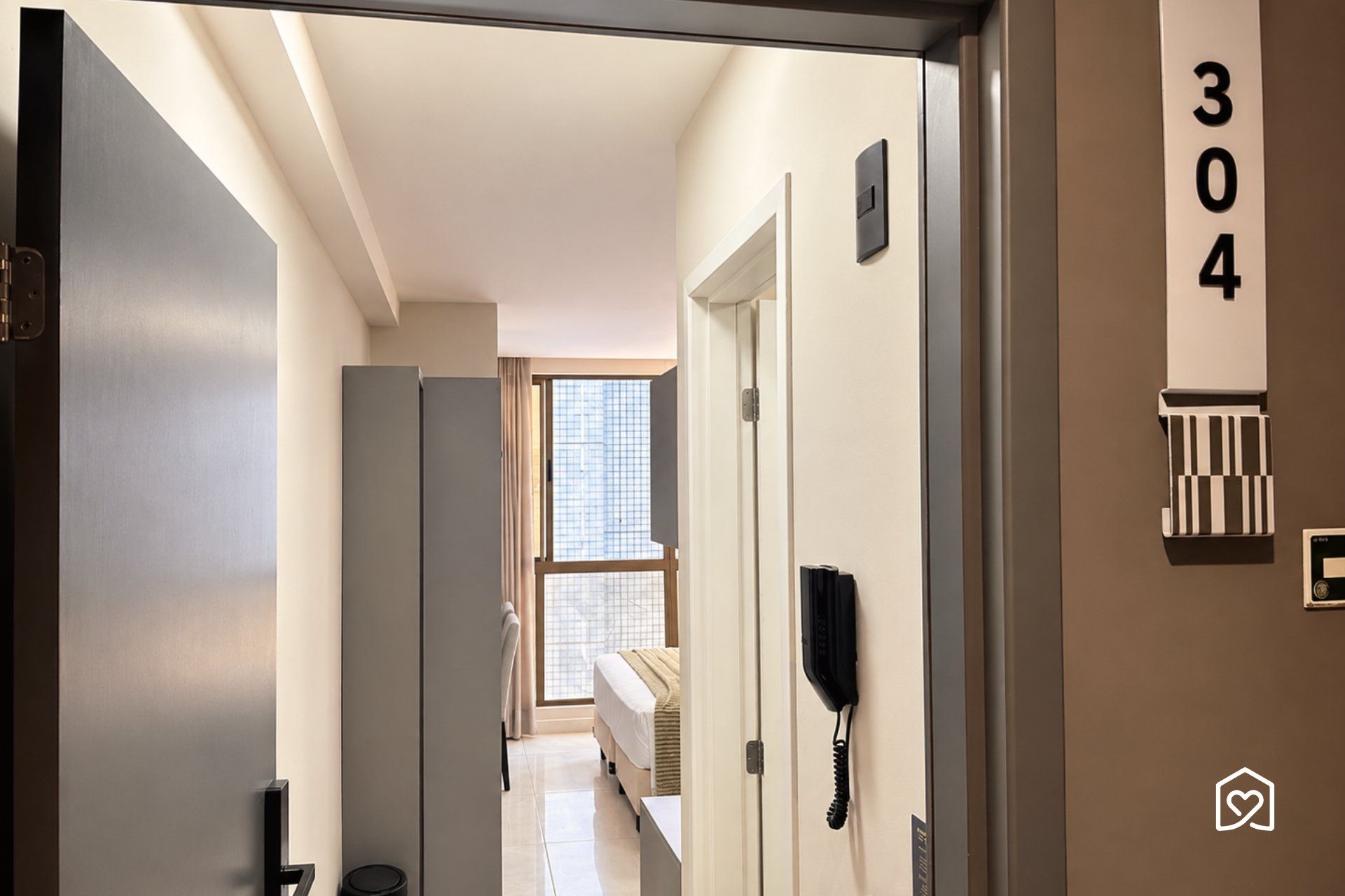 Un pasillo de hotel con una cama, un teléfono y una puerta con el número 304.