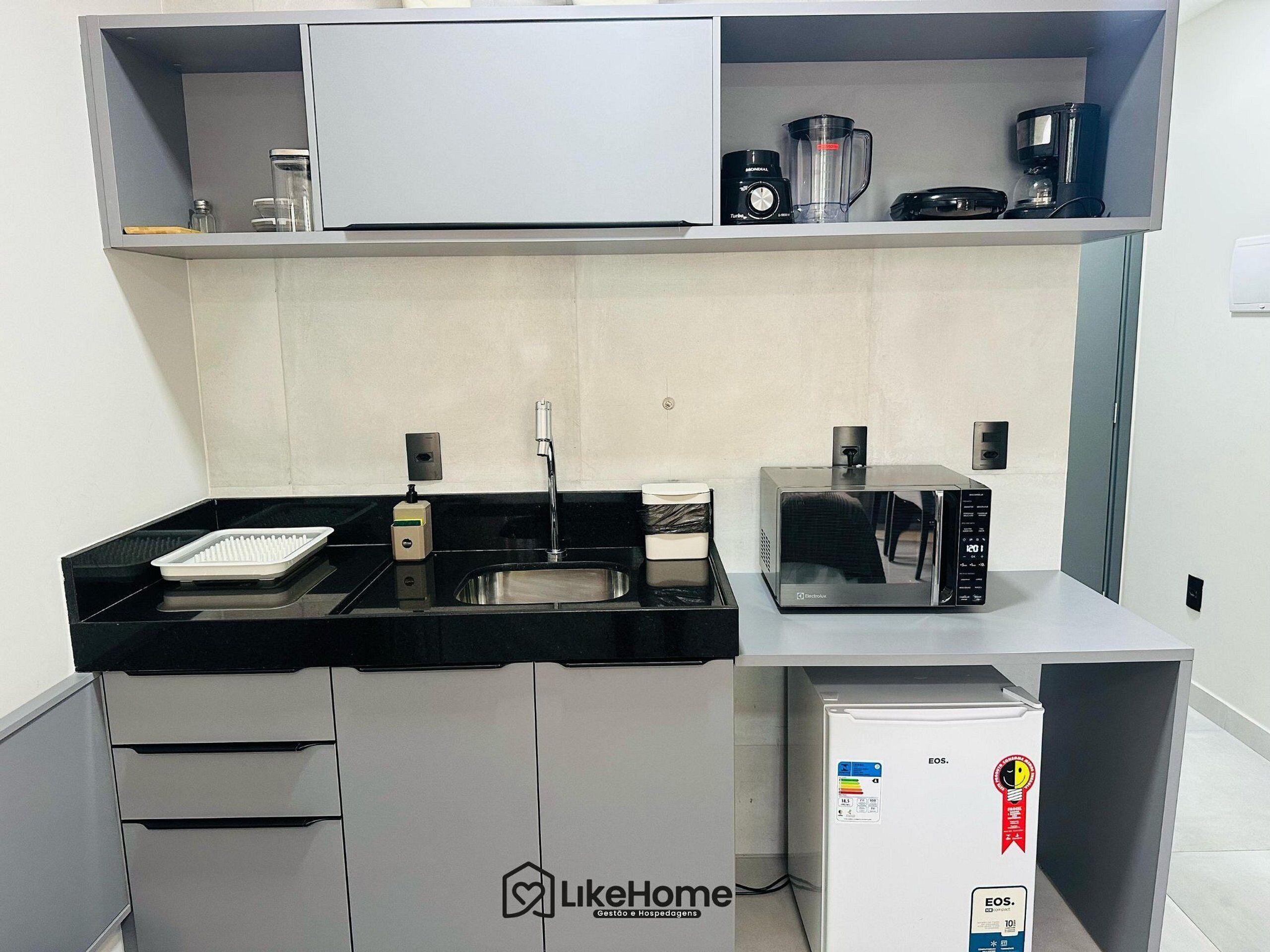 A compact kitchen with a sink, a coffee maker, a blender, and a microwave.