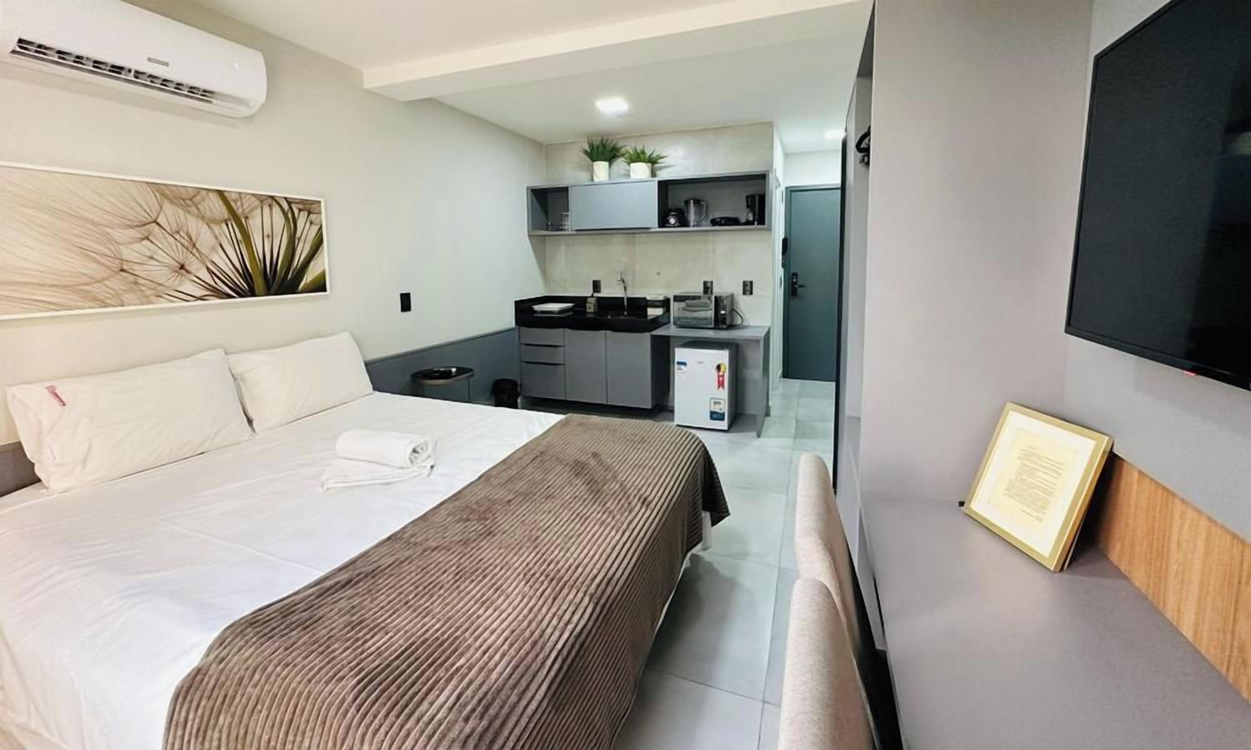 A hotel room with a bed, a small kitchenette, a flat-screen TV, and a framed certificate on the wall.
