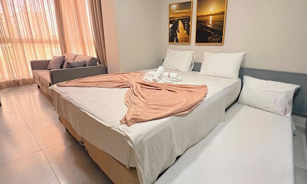 A hotel room with a large bed, a sofa, and two paintings on the wall.