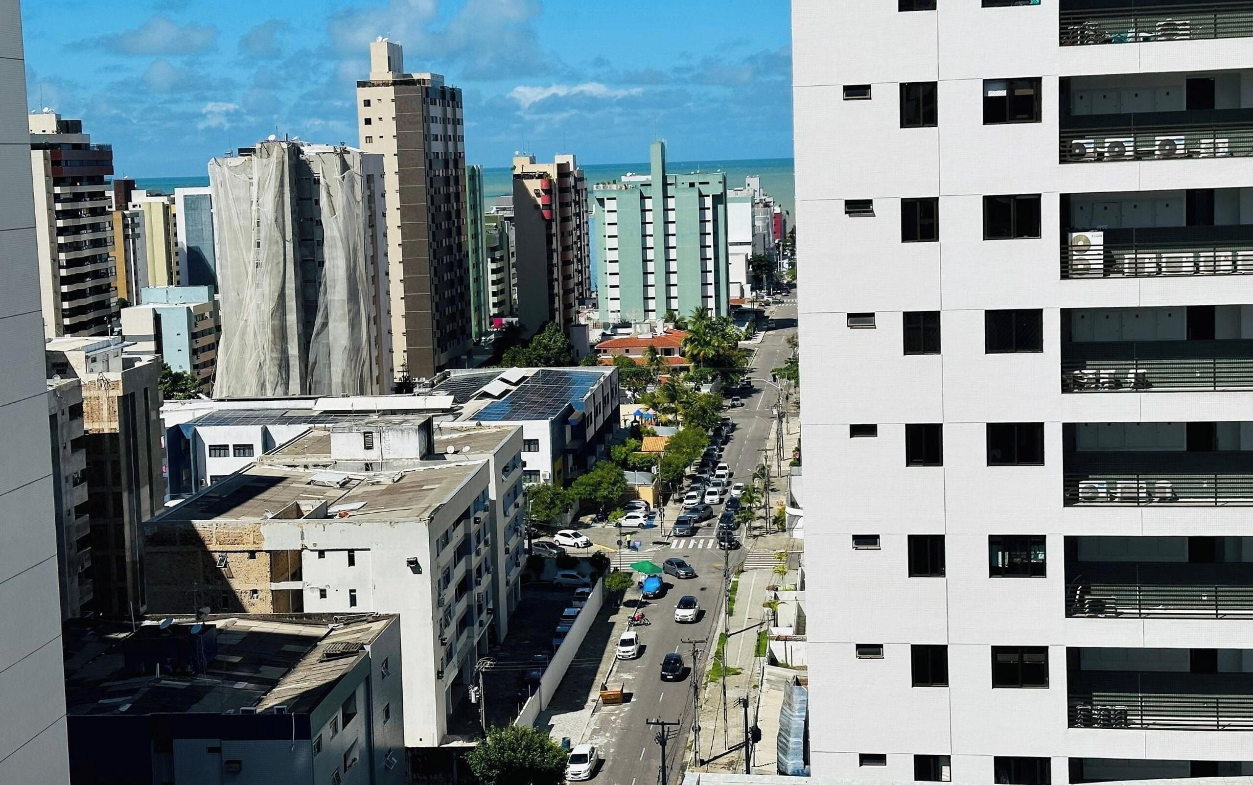A cityscape with high-rise buildings, a clear sky, and a street with parked cars.