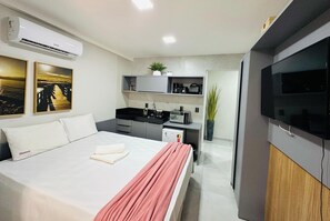 A modern hotel room with a bed, a flat-screen TV, a kitchenette, and a bathroom. - Co-House (João Pessoa)