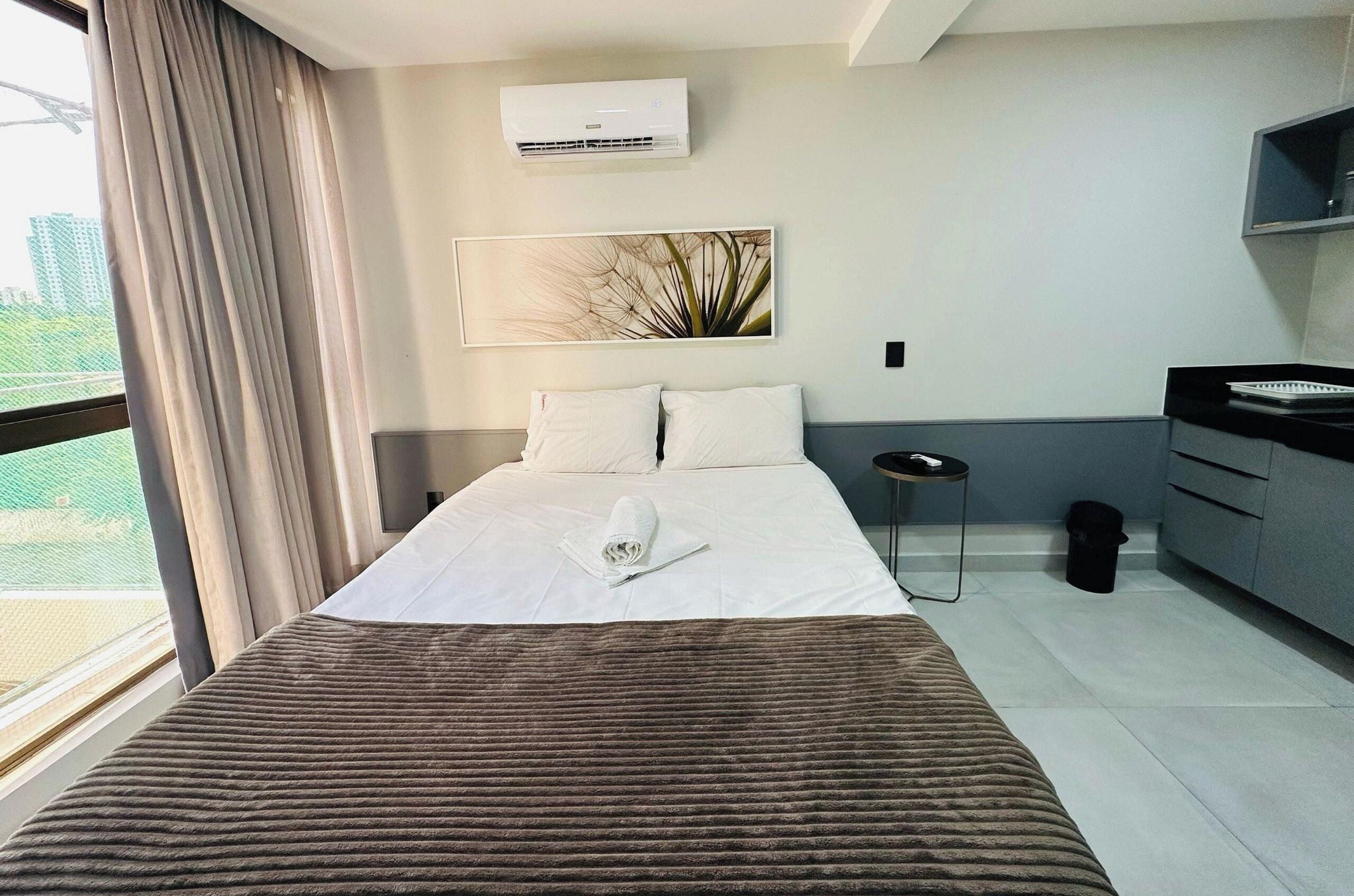 Una habitación de hotel con una cama, un escritorio, una silla y un ventanal con cortinas.
