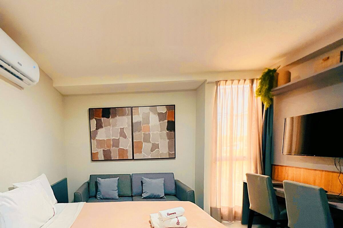 Una habitación de hotel con cama, sofá, televisión y aire acondicionado.