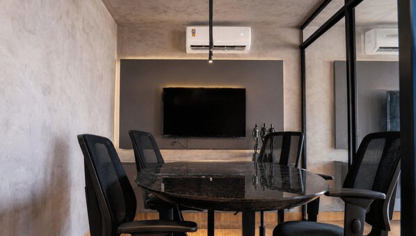 A conference room with a glass table, black chairs, a mounted TV, and an air conditioning unit. - Co-House (João Pessoa)