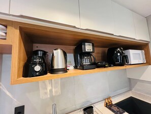 Una cocina con un estante de madera que contiene una cafetera, un hervidor, un microondas y un tostador.