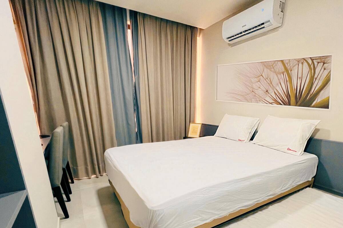 Una habitación de hotel con cama, mesita de noche, aire acondicionado y ventana con cortinas.