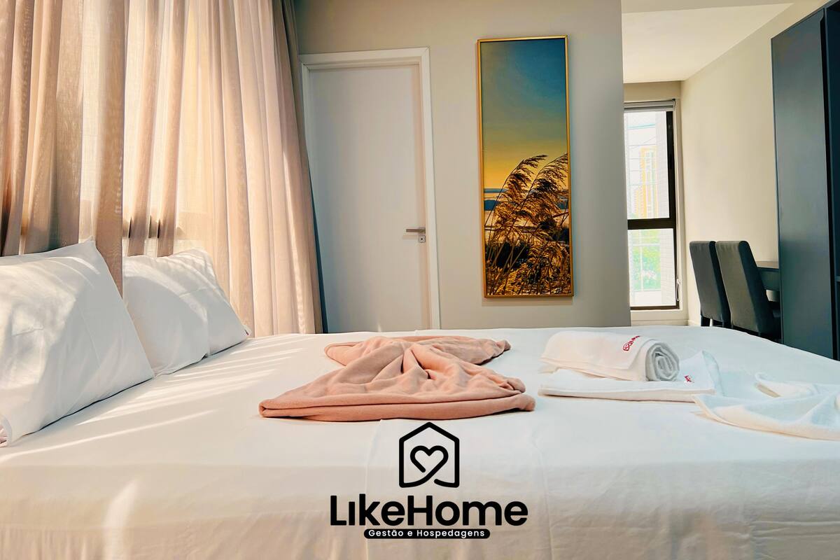 Habitación de hotel con una cama bien hecha, un cuadro en la pared y vistas al exterior por una ventana.