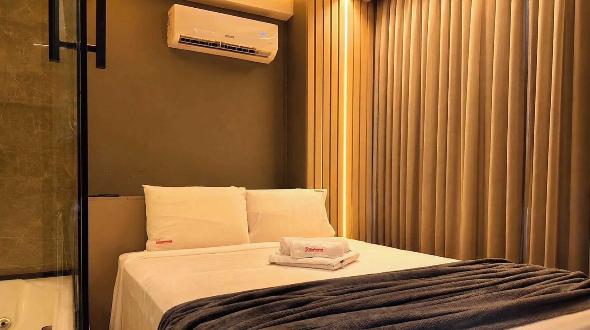 Habitación de hotel con cama, almohadas, una colcha, unidad de aire acondicionado y una cortina.