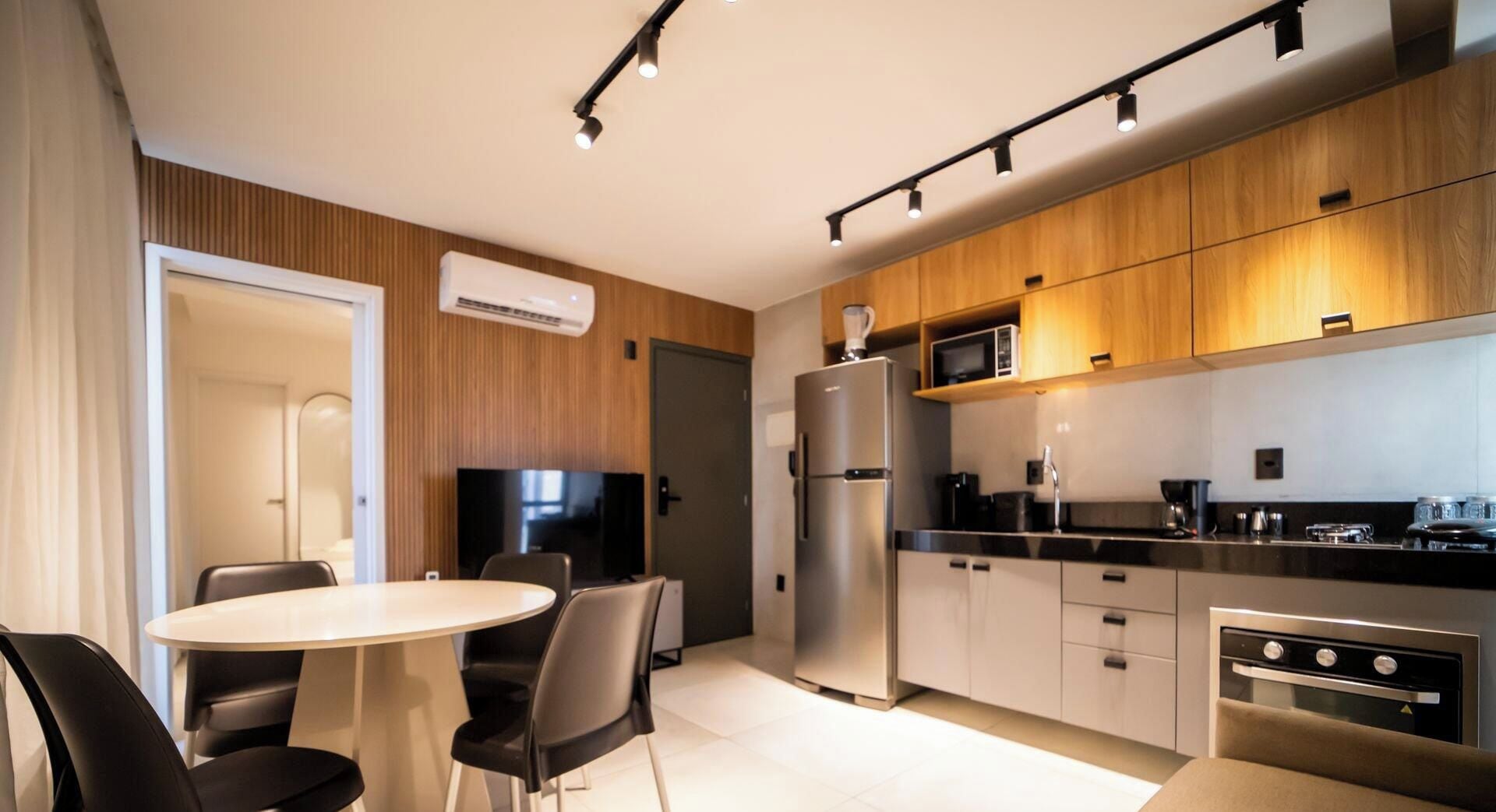 Una cocina moderna con microondas integrado, refrigerador y horno. Hay una mesa de comedor con sillas y un televisor de pantalla plana montado en la pared.