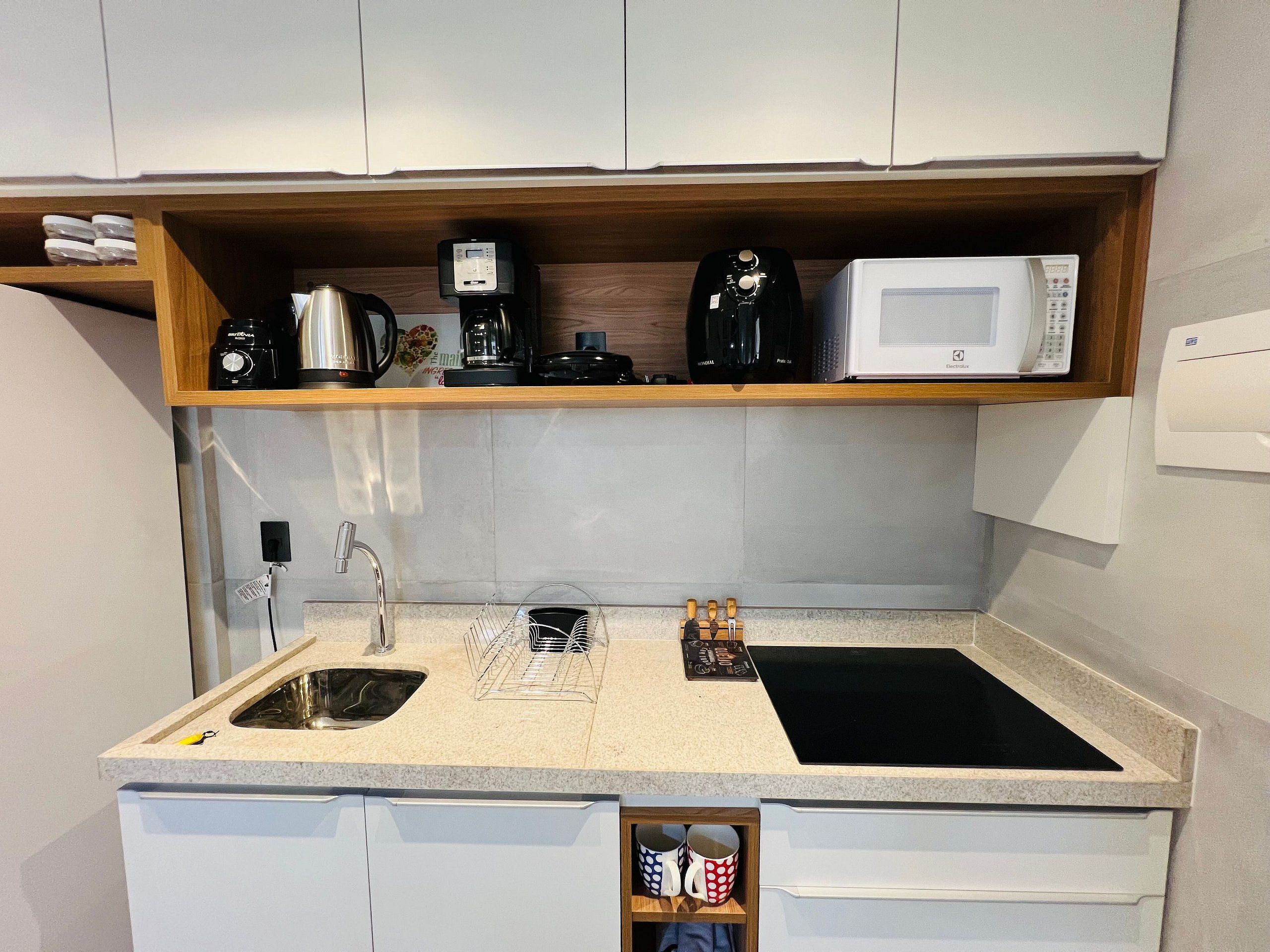 Una cocina compacta con microondas integrado, cafetera y un lavamanos pequeño.