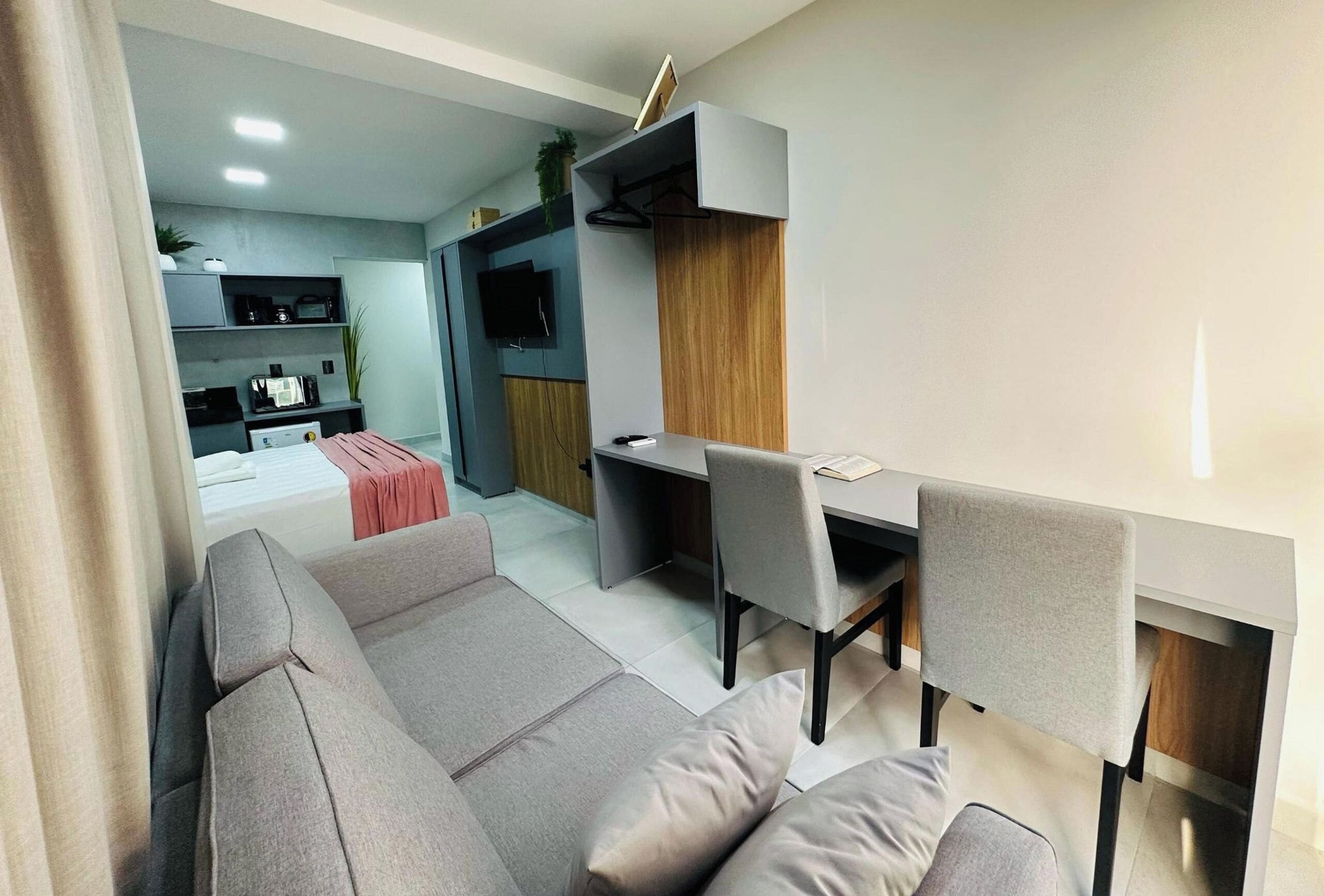 A modern living room with a sofa, a dining table with chairs, a TV, and a kitchen area with cabinets and a microwave.