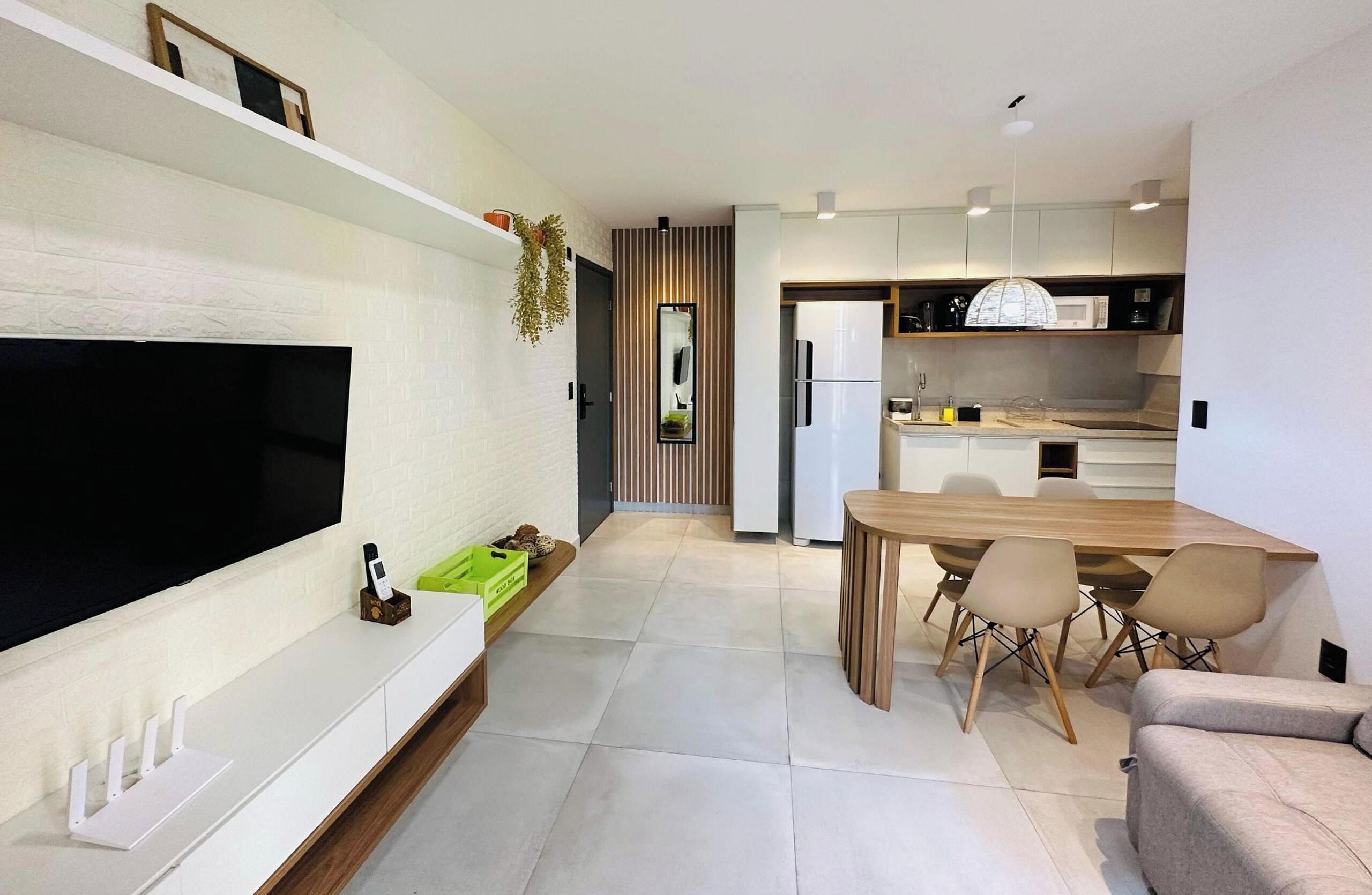 A modern kitchen with a dining area, a flat-screen TV mounted on the wall, and a wooden dining table with chairs.