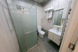 Een badkamer met een douchecabine van glas, een toilet en een wastafel met een spiegel erboven.