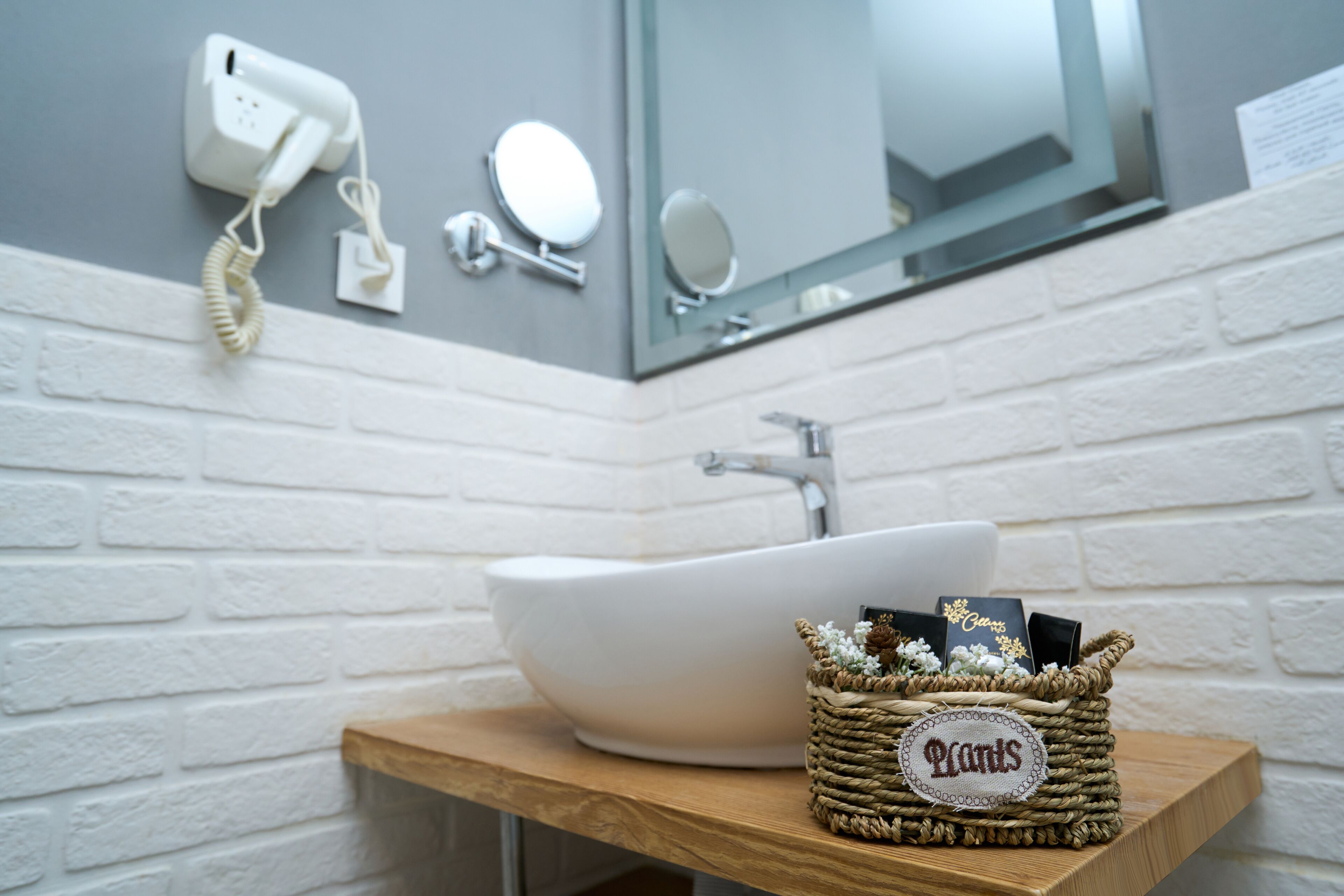 Un baño con un lavamanos blanco, una encimera de madera, una cesta tejida con una etiqueta y un espejo sobre el lavamanos.
