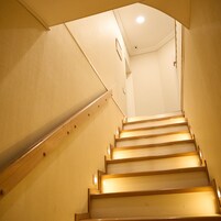Uma escadaria com degraus e corrimãos de madeira, subindo em um espaço interno bem iluminado.
