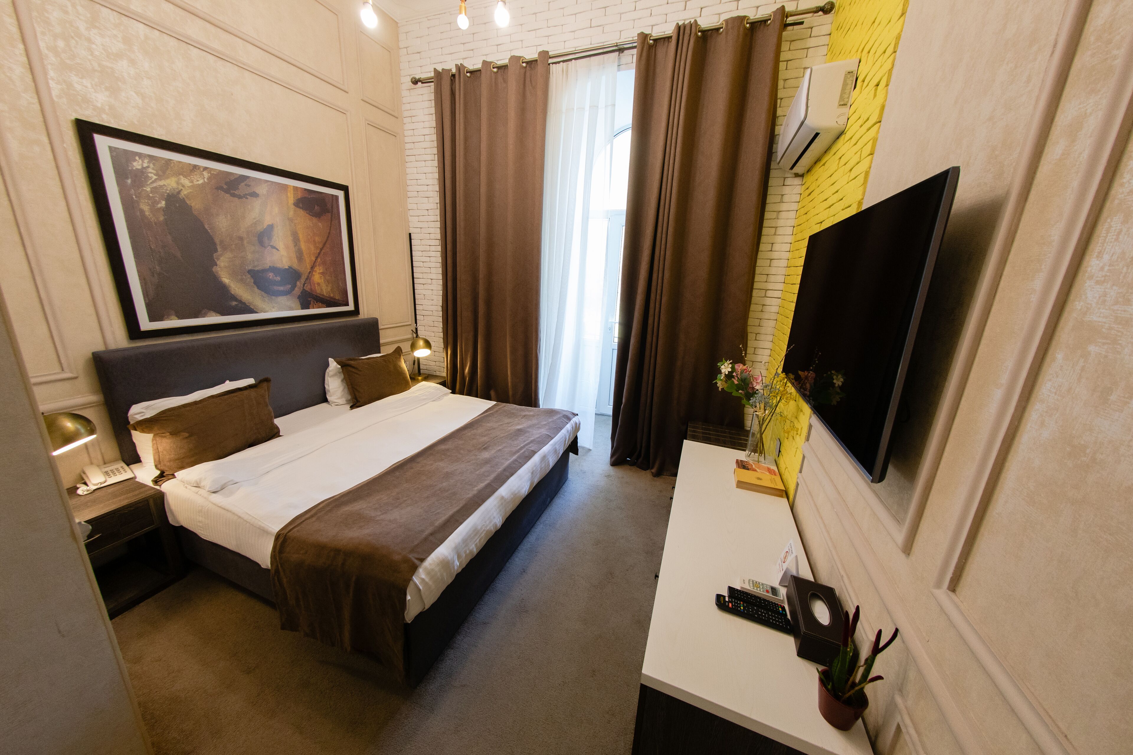 A hotel room with a bed, bedside tables, a TV, and a large painting on the wall.