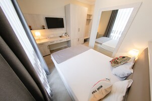 Een hotelkamer met een bed, een bureau met lamp, een kledingkast, een televisie en een grote spiegel.